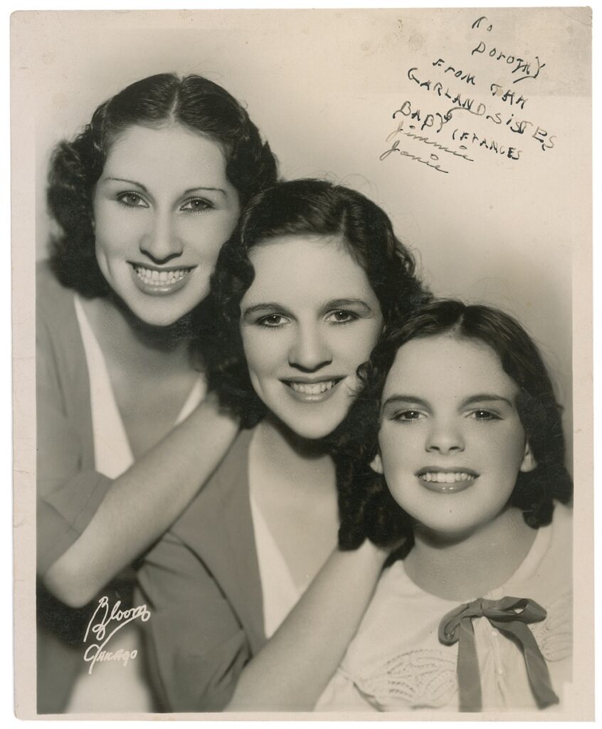 An early photo of Garland posing with her older sisters. The inscription reads, "To Dorothy from the Garland Sistes [sic], Baby Frances" and signed by both her sisters "Jimmie," and "Janie."