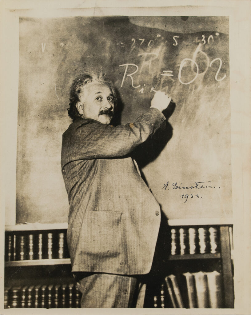 Einstein writing an equation on a chalkboard.