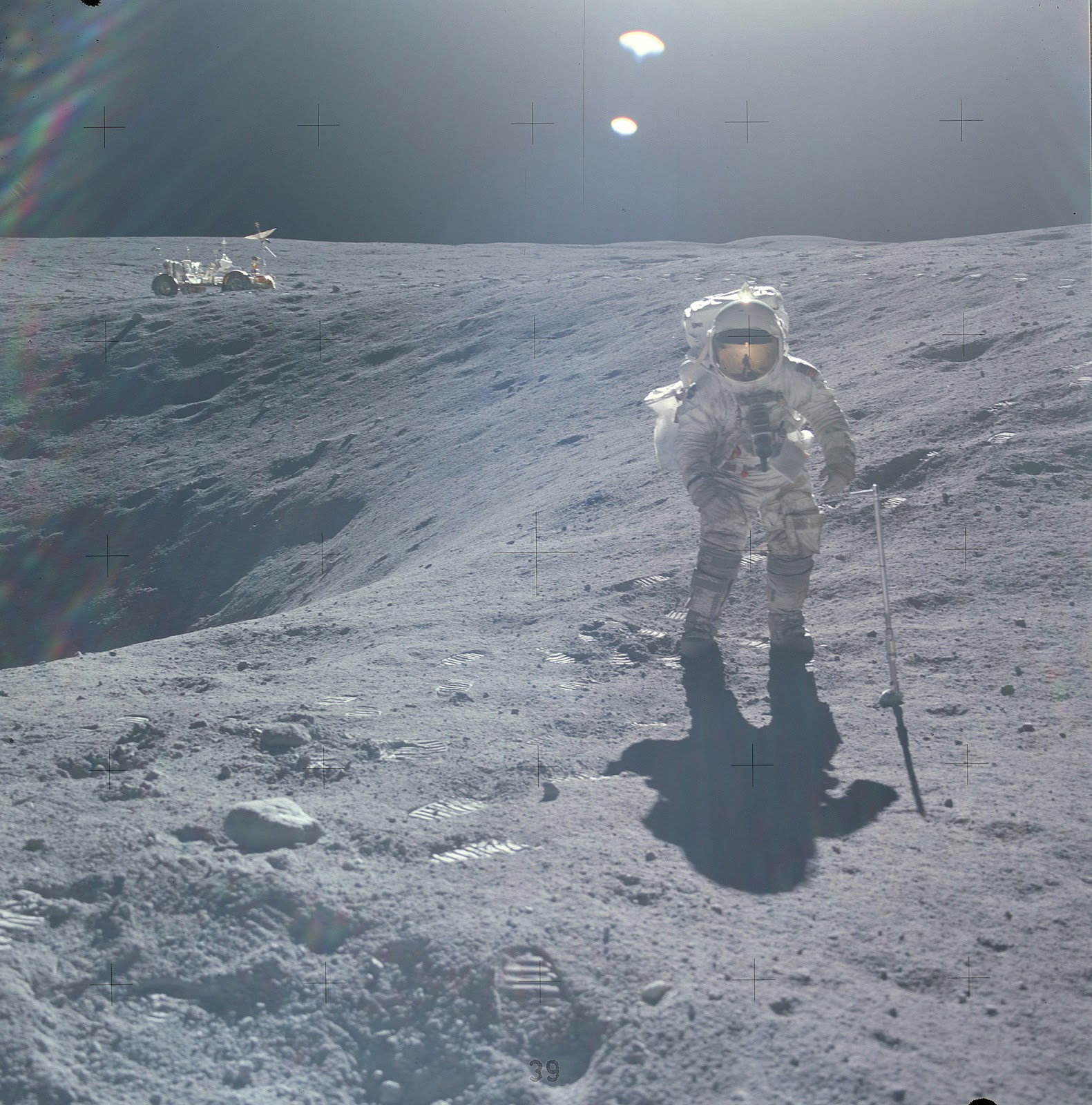 Charlie Duke photographed on the lunar surface with the moon rock scoop at his side. The scoop is attached to a pole segment to extend its length.