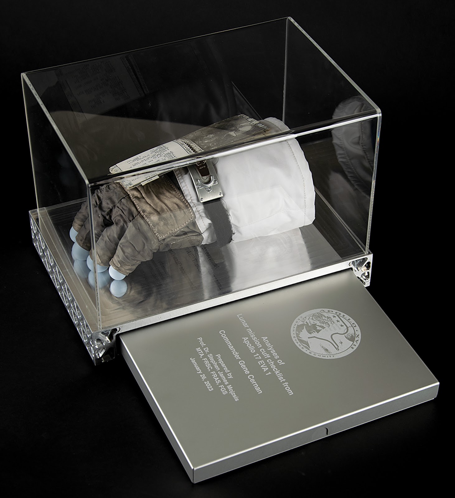 The cuff checklist displayed with an aluminum case engraved with the Apollo 17 mission insignia. Inside of this case are documents including Gene Cernan’s provenance document and a report on the lunar dust by Dr. Stephen J. Mojzsis. 