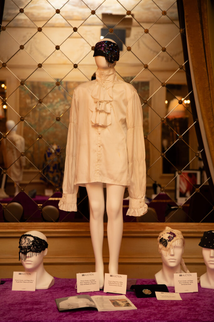 Prince’s stage-worn ruffled shirt from his performance of Purple Rain at the 1985 American Music Awards displayed on a mannequin beside the brooch also worn at the performance and several of Prince’s head scarfs.